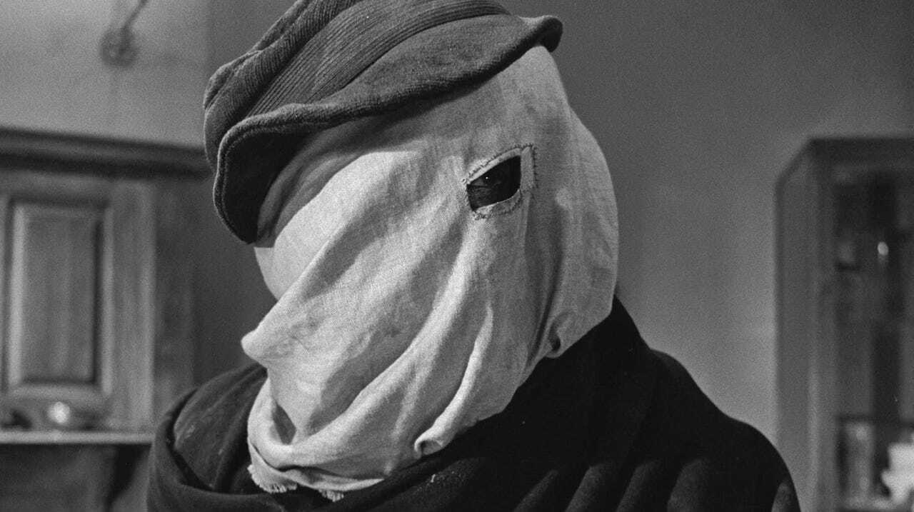 still from The Elephant Man (1980) - a black and white image of a man in close-up with a sack over his head, only one eye is visible through a rectangular hole